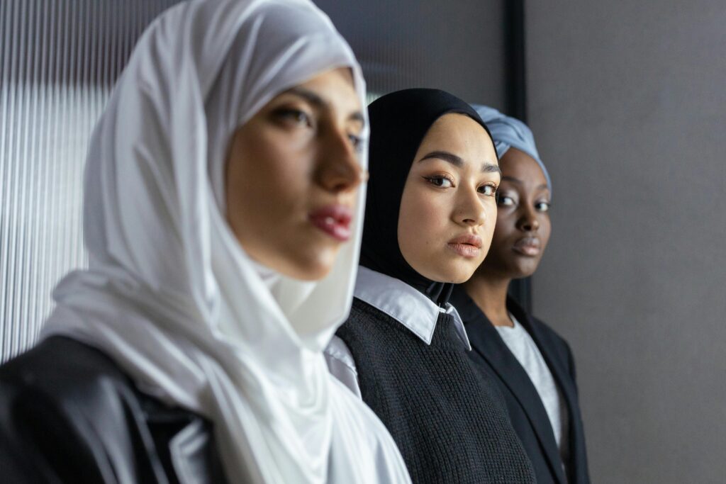 Three diverse women wearing hijabs pose confidently indoors, representing multicultural beauty and strength.