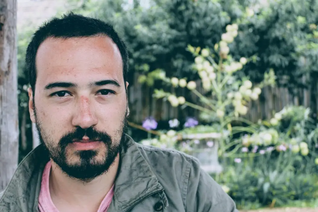 Portrait of a young man with facial hair, outdoors in a natural setting. Serious expression.